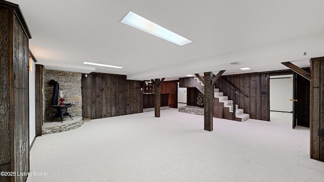 basement with wooden walls, light colored carpet, and a wood stove