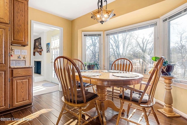 dining space with plenty of natural light, dark wood-type flooring, a chandelier, and a brick fireplace