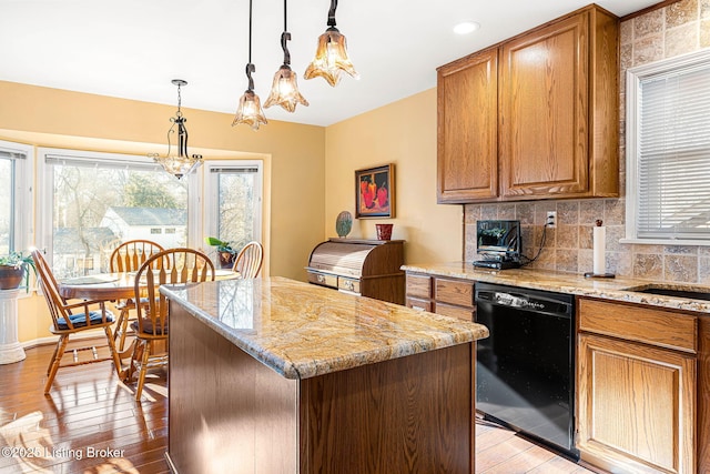 kitchen with light stone counters, light hardwood / wood-style flooring, dishwasher, a kitchen island, and pendant lighting