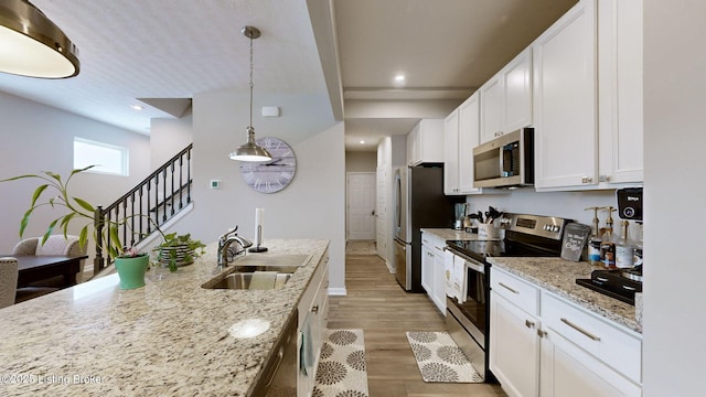 kitchen with sink, stainless steel appliances, light stone counters, pendant lighting, and white cabinets