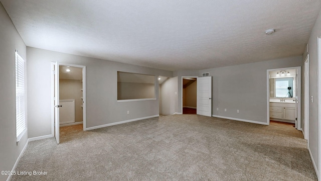 unfurnished bedroom featuring a textured ceiling, ensuite bath, light carpet, and multiple windows