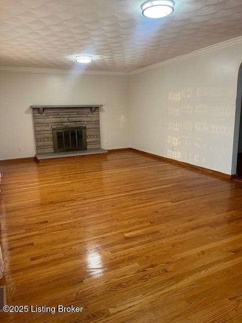 unfurnished living room with a textured ceiling, ornamental molding, hardwood / wood-style floors, and a stone fireplace