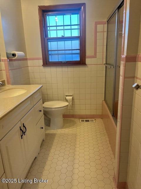 full bathroom featuring shower / bath combination with glass door, tile patterned floors, vanity, tile walls, and toilet