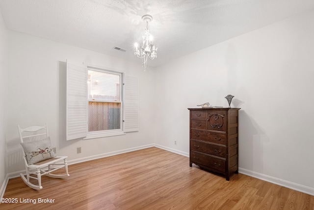 spare room featuring a textured ceiling, light wood-type flooring, and an inviting chandelier