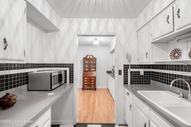 kitchen featuring sink, light hardwood / wood-style floors, decorative backsplash, and white cabinetry