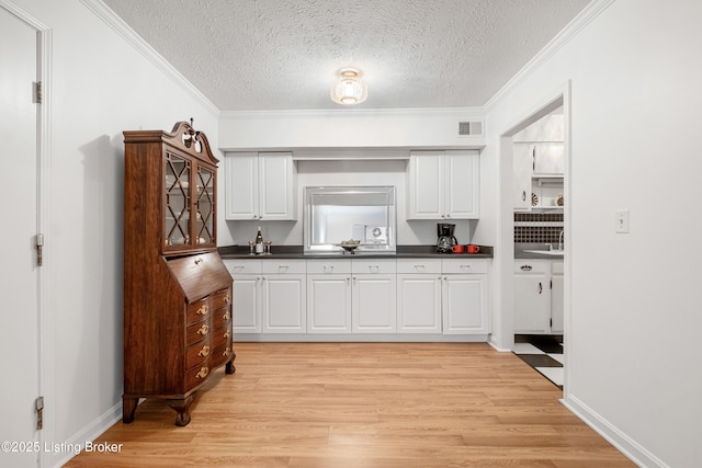 kitchen with white cabinetry, a textured ceiling, and crown molding