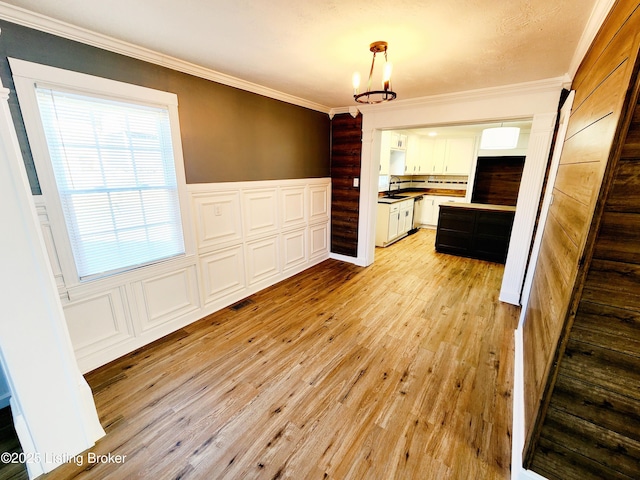 kitchen featuring pendant lighting, white cabinets, ornamental molding, an inviting chandelier, and light hardwood / wood-style flooring