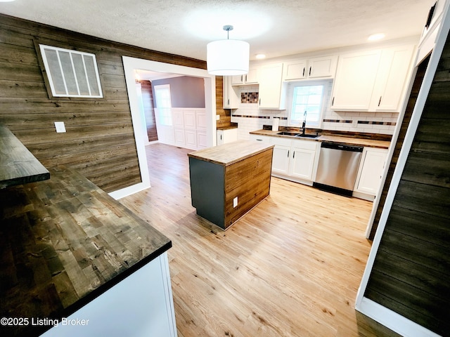 kitchen with pendant lighting, light hardwood / wood-style floors, white cabinets, a kitchen island, and stainless steel dishwasher