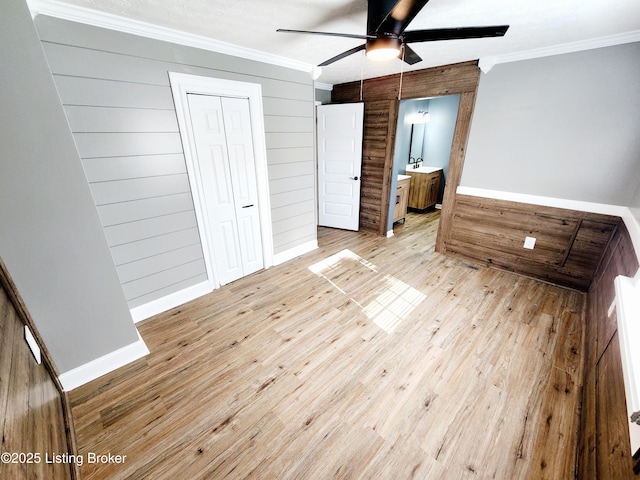 unfurnished bedroom with ensuite bath, ceiling fan, ornamental molding, light wood-type flooring, and wood walls