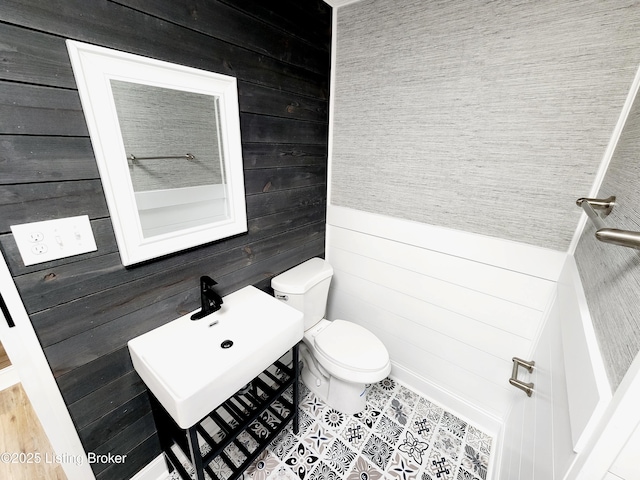 bathroom with sink, toilet, and wood walls