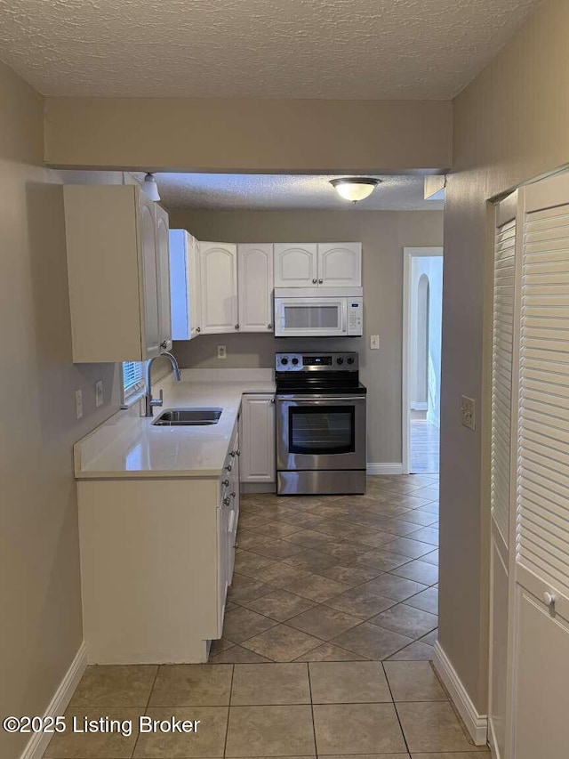 kitchen with stainless steel range with electric stovetop, light tile patterned flooring, white cabinets, and sink