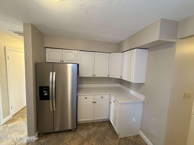 kitchen with white cabinetry, stainless steel fridge, light tile patterned flooring, and a textured ceiling