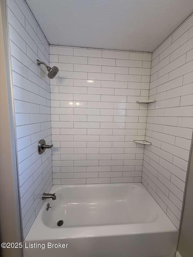 bathroom featuring a textured ceiling and tiled shower / bath