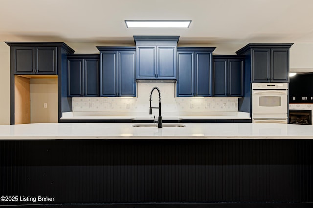 kitchen featuring a center island with sink, blue cabinets, sink, decorative backsplash, and double oven