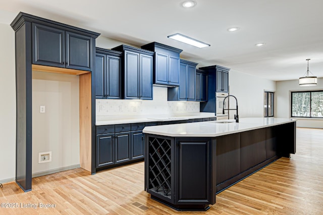 kitchen featuring blue cabinetry, sink, an island with sink, and light hardwood / wood-style floors