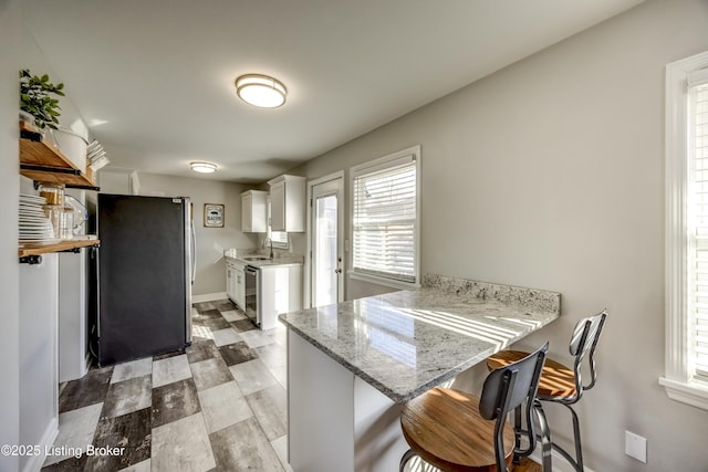 kitchen featuring light stone counters, kitchen peninsula, white cabinetry, appliances with stainless steel finishes, and a kitchen breakfast bar