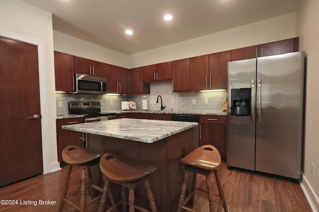 kitchen featuring a kitchen island, stainless steel appliances, a kitchen breakfast bar, and dark hardwood / wood-style floors