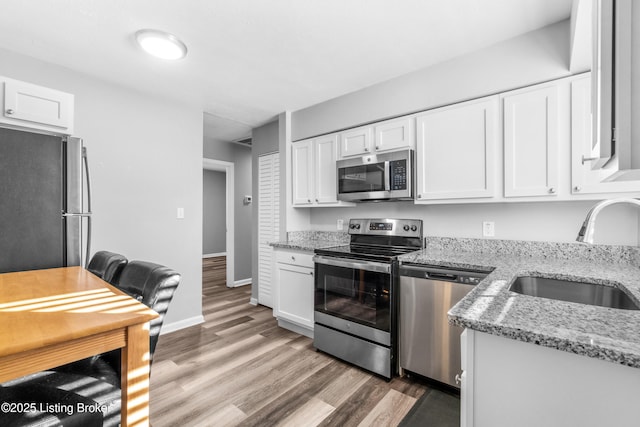 kitchen featuring wood-type flooring, sink, stainless steel appliances, white cabinets, and light stone counters