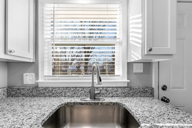 interior details featuring white cabinets, sink, and light stone counters