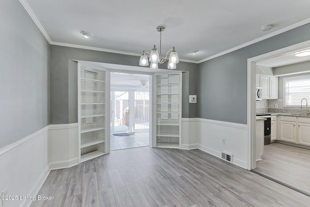 unfurnished dining area with ornamental molding, light hardwood / wood-style floors, sink, and a notable chandelier