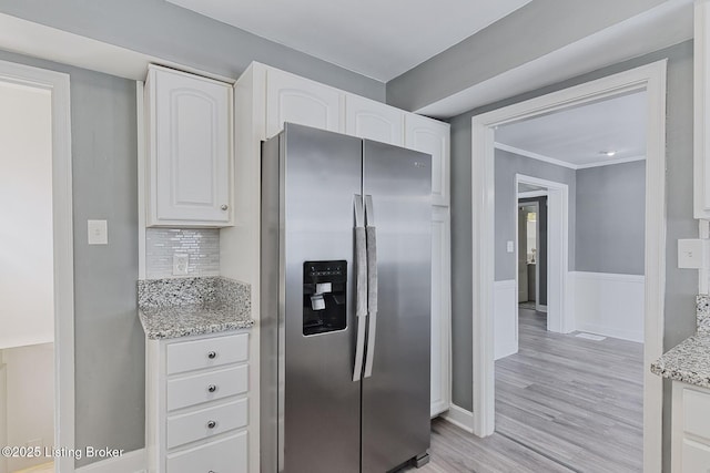 kitchen with white cabinetry, backsplash, stainless steel fridge, light stone counters, and light hardwood / wood-style floors