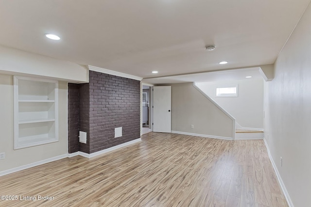 basement with brick wall, built in features, and light wood-type flooring