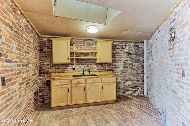 kitchen with brick wall, sink, and light brown cabinetry