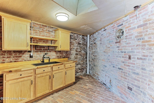 kitchen featuring brick wall, sink, wooden counters, and light brown cabinetry