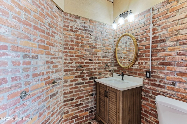 bathroom featuring vanity, brick wall, and toilet