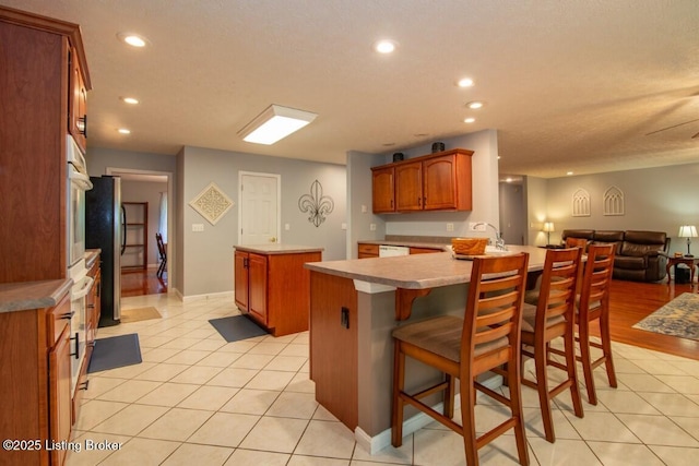 kitchen featuring a textured ceiling, a kitchen bar, light tile patterned floors, kitchen peninsula, and stainless steel refrigerator