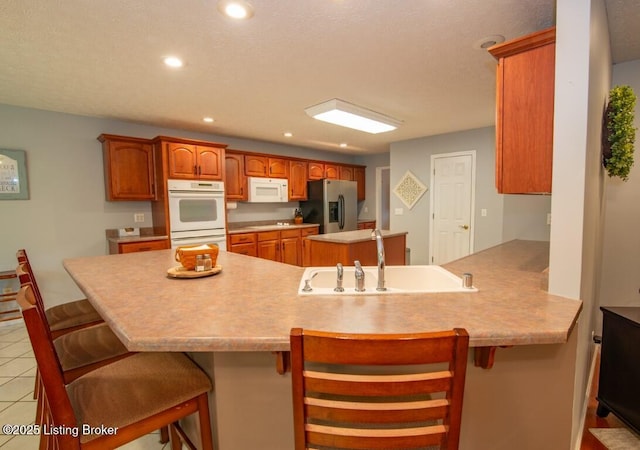 kitchen featuring white appliances, a kitchen breakfast bar, kitchen peninsula, light tile patterned floors, and sink