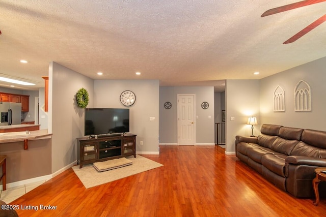 living room with a textured ceiling, ceiling fan, and light wood-type flooring