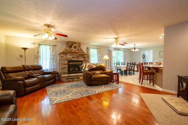 living room with a textured ceiling, ceiling fan, light hardwood / wood-style floors, and a stone fireplace