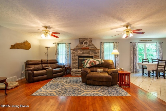 living room with a textured ceiling, ceiling fan, hardwood / wood-style floors, and a fireplace