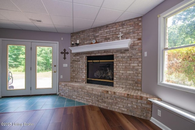 unfurnished living room with a brick fireplace, a drop ceiling, and hardwood / wood-style flooring