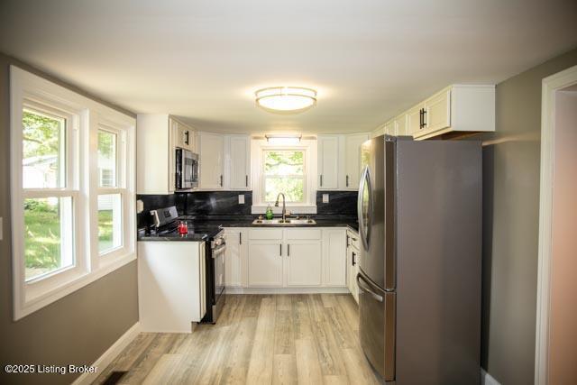 kitchen featuring stainless steel appliances, sink, white cabinets, tasteful backsplash, and light hardwood / wood-style flooring