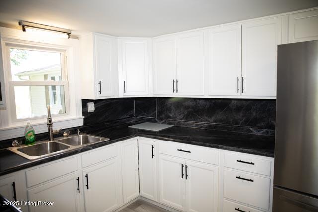 kitchen featuring sink, stainless steel fridge, white cabinetry, and tasteful backsplash