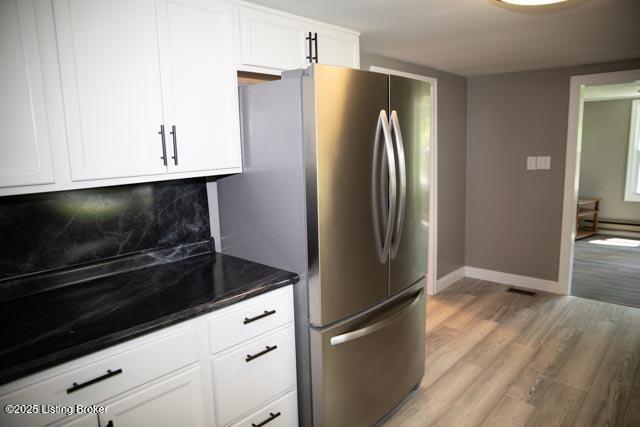 kitchen featuring stainless steel fridge, light hardwood / wood-style floors, backsplash, white cabinetry, and dark stone countertops