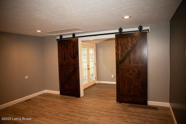 spare room with french doors, a textured ceiling, hardwood / wood-style flooring, and a barn door