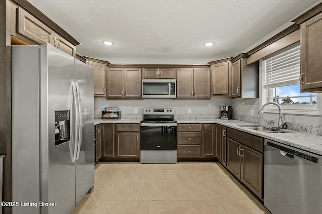 kitchen featuring appliances with stainless steel finishes, light stone counters, dark brown cabinetry, and sink