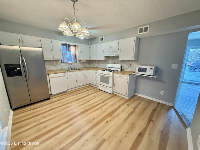 kitchen with white appliances, hanging light fixtures, and white cabinets