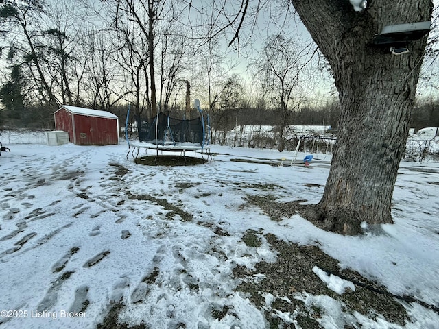 yard layered in snow with a storage unit and a trampoline