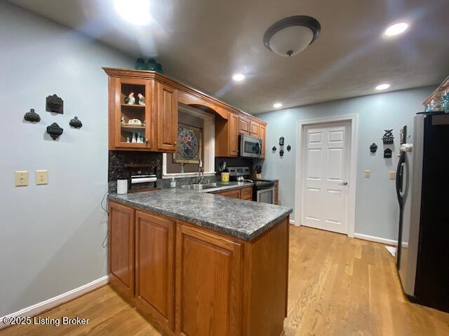 kitchen with sink, light wood-type flooring, kitchen peninsula, and appliances with stainless steel finishes