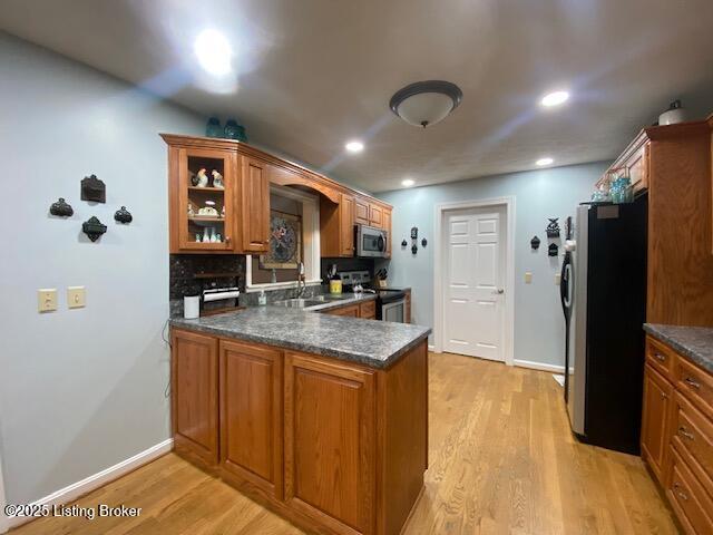 kitchen with appliances with stainless steel finishes, kitchen peninsula, sink, and light hardwood / wood-style flooring