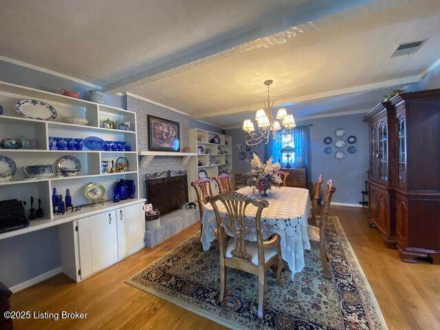 dining area with beamed ceiling, ornamental molding, a notable chandelier, and light hardwood / wood-style floors