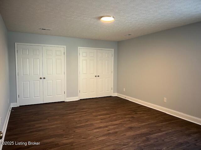 unfurnished bedroom with dark wood-type flooring, multiple closets, and a textured ceiling