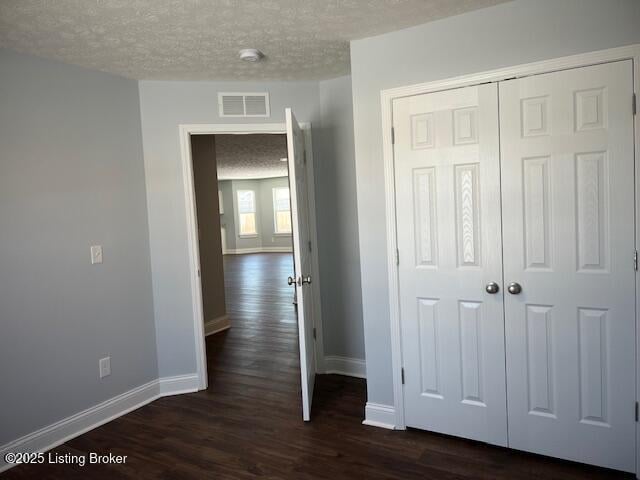 unfurnished bedroom featuring a textured ceiling, dark hardwood / wood-style floors, and a closet