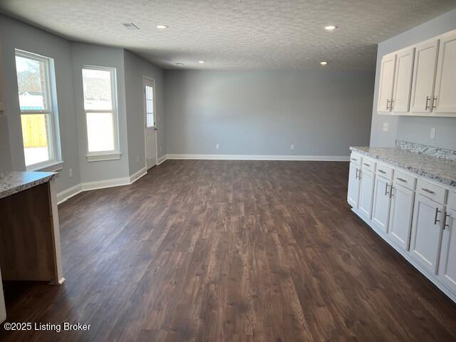 interior space featuring a textured ceiling, dark wood-type flooring, white cabinetry, and light stone counters