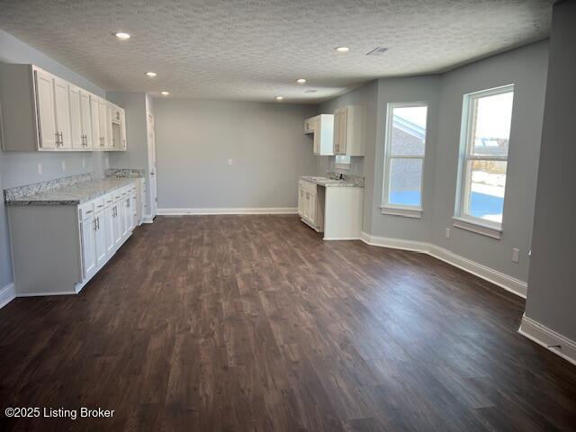 kitchen with a textured ceiling, dark hardwood / wood-style flooring, white cabinets, and light stone countertops