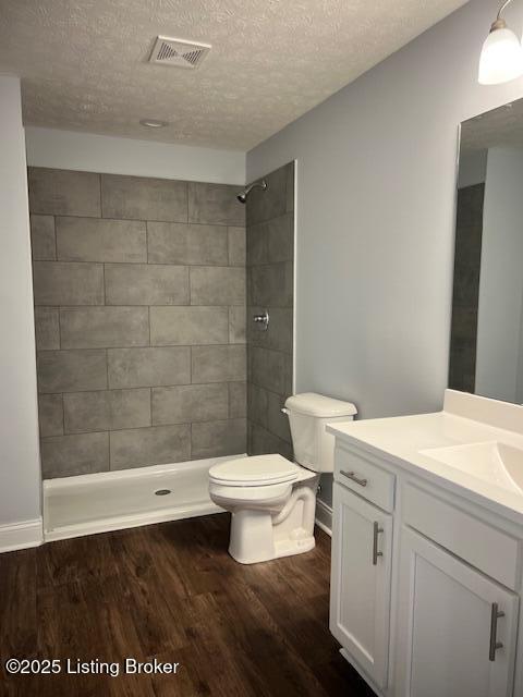 bathroom featuring hardwood / wood-style flooring, toilet, vanity, and a tile shower